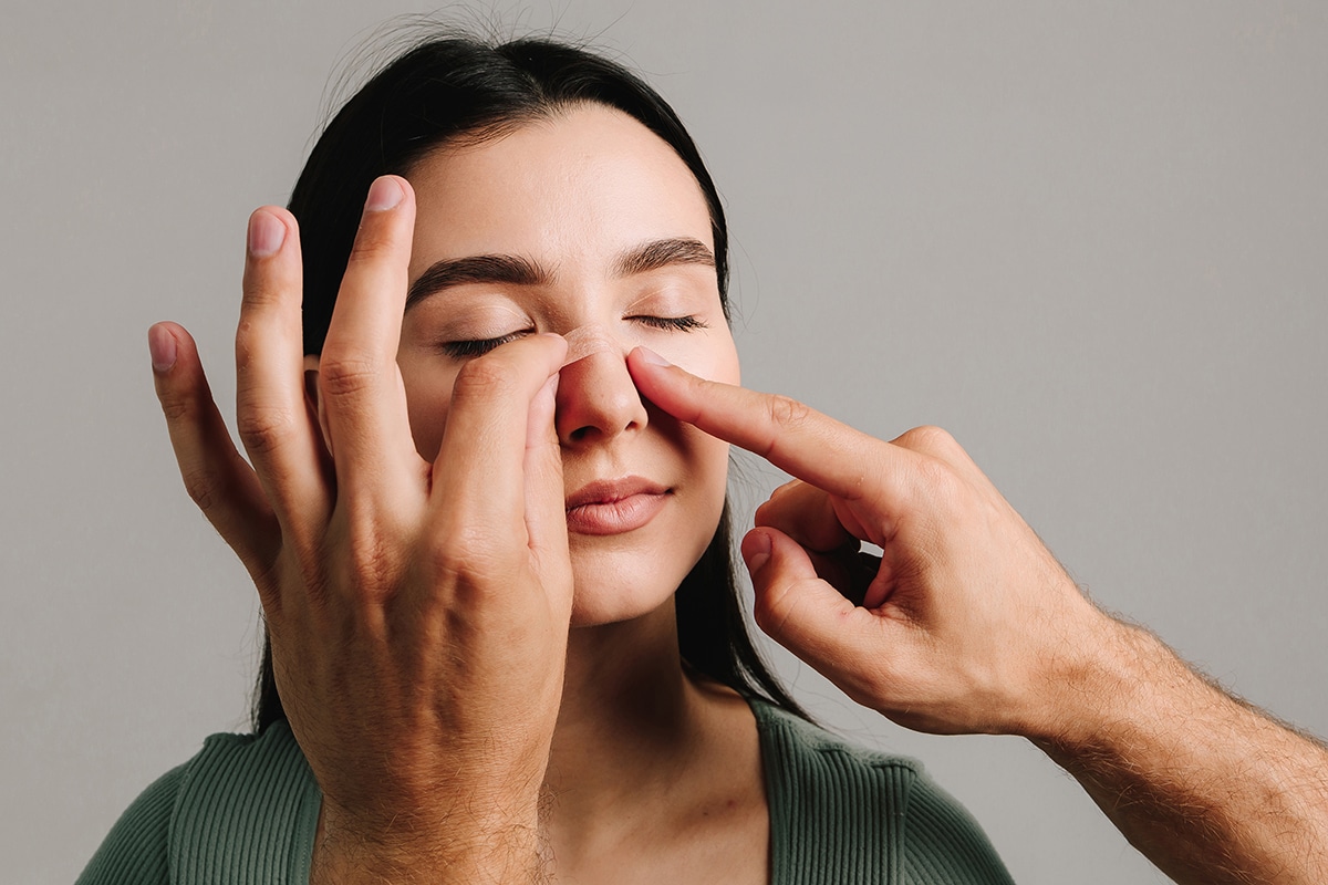 Woman with eyes closed as hands apply a nasal strip to her nose.