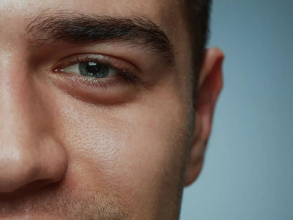 Close-up of a man's blue eye and skin texture showing pores and eyelashes for skincare or ophthalmology.