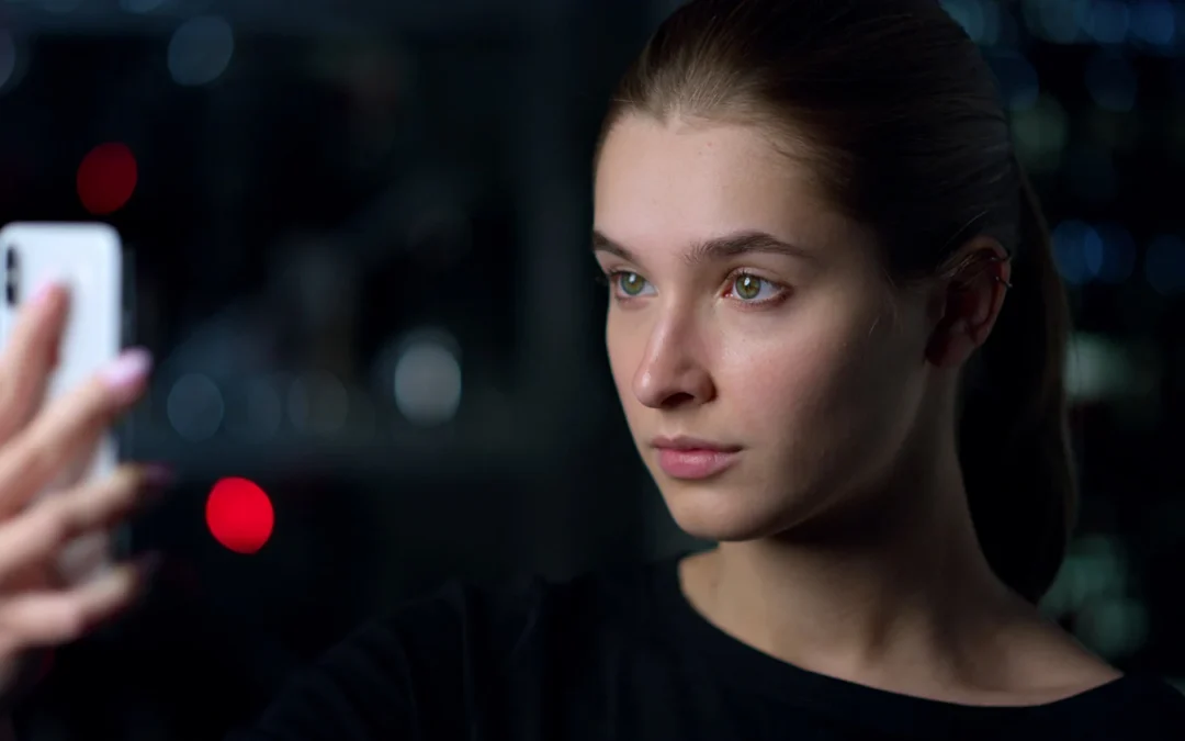 Young woman with green eyes using a white smartphone at night with city bokeh background.